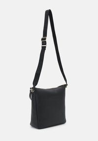 Sac bandoulière rectangulaire en cuir noir avec une large sangle ajustable, avec un logo embossé et des accessoires métalliques dorés.