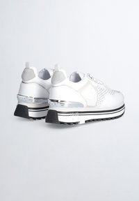 Sneakers bianche con dettagli in mesh, accenti grigi, un tacco in cromo e una suola nera testurizzata. Presentano lacci e un logo di branding sul lato.