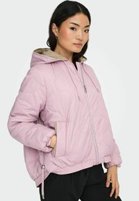 Rosa vattert jakke med hette, med lyst beige fôr, elastiske mansjetter og glidelåslommer foran. Designet har en myk tekstur.