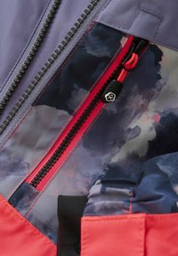 Wasserabweisende Jacke mit lila Außenseite, mehrfarbigem Innenfutter und kontrastierendem roten Reißverschluss. Texturiertes Gewebe und einfarbige Akzente sichtbar.