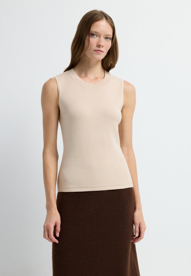 Beige mouwloos topje met een ronde halslijn, gemaakt van zachte stof, gecombineerd met een bruin gestructureerd wollen rok. Eenvoudig en aansluitend ontwerp.