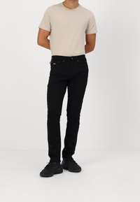 Zwarte jeans met een slim fit, gecombineerd met een beige crew neck t-shirt. De jeans hebben een five-pocket ontwerp en subtiele branding op de tailleband.