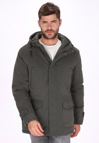 Chaqueta acolchada de color verde oliva con capucha, que cuenta con una cremallera frontal, dos bolsillos laterales y una textura suave. Puños reforzados con broches.