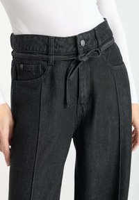 Zwarte denim broek met een hoge taille en verstelbaar trekkoord. Bevat zijzakken en een gladde textuur met subtiele stiksels.