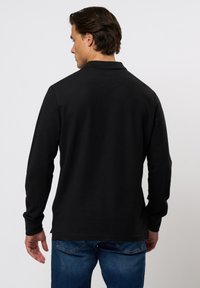 Svart langermet genser med teksturert overflate, avslappet passform og en subtil krage, kombinert med blå denimjeans.