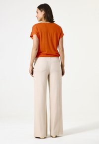 Top corto de color naranja oxidado con un ajuste relajado, combinado con pantalones de pierna ancha de color beige claro que cuentan con dos bolsillos traseros y una textura suave.