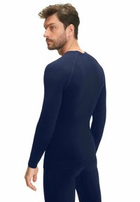 Marineblauw lang mouwtop met een aansluitend ontwerp, gemaakt van textuurstof. Bevat ribbelaccenten op de schouders en een glad paneel op de achterkant.
