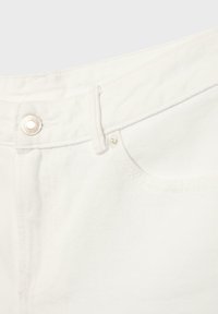 Gros plan sur un jean en denim blanc avec un bouton en métal, une passoire de ceinture et des coutures visibles de la poche avant.