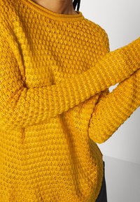 Maglione giallo lavorato a maglia con un motivo testurizzato, caratterizzato da un collo rotondo e maniche lunghe, con polsini a coste e un fit over.