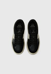 Sneakers din piele neagră cu accente crem, având un design cu șireturi, vârf rotund și o talpă exterioară texturată. Logo vizibil pe limba încălțămintei.