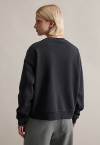 Ciemnoszara bluza z okrągłym dekoltem, z opuszczonymi ramionami i ściągaczami na rękawach. Wykonana z mieszanki bawełny, o luźnym kroju, gładka, bez widocznych wzorów.