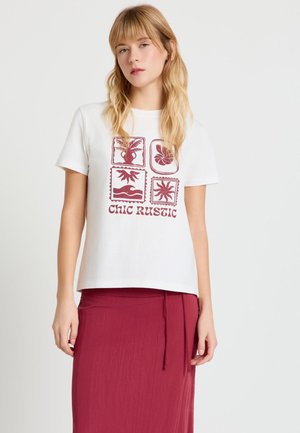 Donna che indossa una t-shirt bianca a maniche corte con stampe rosse a tema naturale e la scritta "CHIC RUSTIC", abbinata a una gonna rossa.