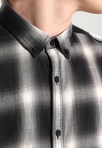 Zwart-wit geblokte shirt met een button-down kraag, voorzien van zwarte knopen en een gestructureerde stof, die een klassiek geruit patroon benadrukt.