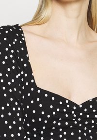 Czarna sukienka w białe kropki, kwadratowy dekolt i marszczenia przy piersiach; wykonana z gładkiego, elastycznego materiału.