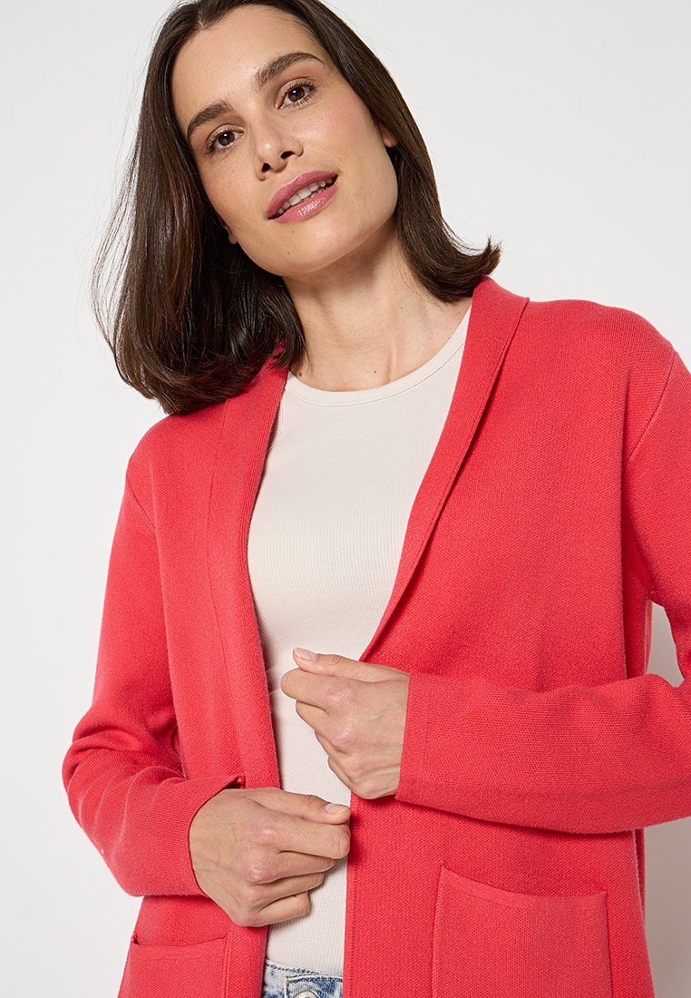 Korallfarbener Cardigan aus einem weichen Strickmaterial mit lässiger Passform, offener Vorderseite, zwei vorderen Taschen und langen Ärmeln.