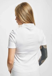 Hvit ribbestrikket poloshirt med korte ermer, med klassisk krage og tettsittende silhuett. Jevn tekstur og subtile vertikale linjer.