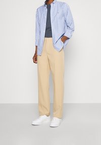 Gestreept blauw-wit overhemd met knopen over een marineblauw t-shirt, gecombineerd met beige broek en witte sneakers. Gestructureerde stof, losse pasvorm.