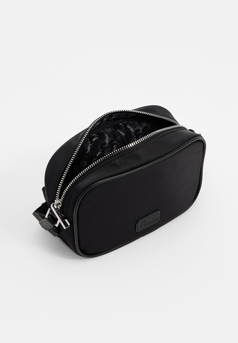 Bolso de maquillaje negro hecho de un tejido duradero, con un exterior suave, cremallera plateada y un forro interior con un patrón. Forma rectangular compacta.