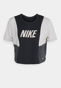 Camiseta recortada de Nike en negro y gris claro, con mangas cortas, que presenta un gran logo blanco en el pecho y un escote redondo.