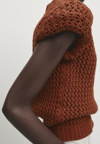 Top lavorato a maglia color ruggine con un design largo e strutturato, maniche corte e orlo a coste, con un braccio in mostra.