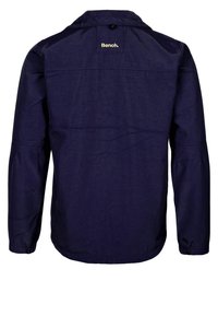 Tmavě modrá bunda s dlouhým rukávem, límcem na knoflíky a elastickými manžetami. Má prošívané švy a logo na horní části zad.