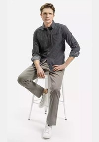 Czarna i biała koszula w kropki z guzikami, szare strukturalne spodnie i białe trampki, siedzący na stołku, podkreślający casualowy styl męski.