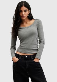 Maglione grigio a maniche lunghe con costine e scollo ampio, abbinato a pantaloni neri a vita alta con chiusura a bottoni e tasche laterali.