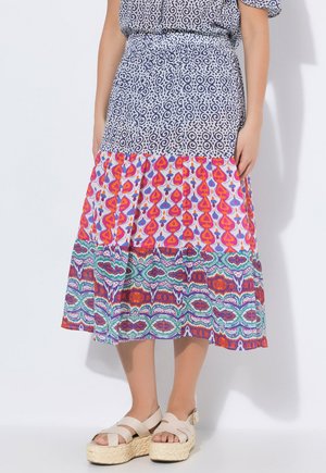 Kvinde iført en midlang nederdel med blå, pink, grønne og orange abstrakte mønstre, kombineret med beige platform-sandaler.