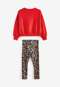 Sweatshirt en coton rouge à manches longues et poignets côtelés, associé à des leggings imprimés léopard dans des nuances de marron et de noir.
