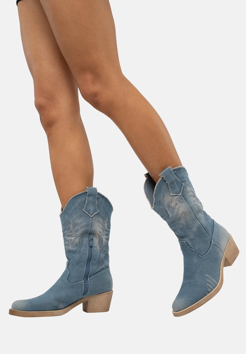 Botas de vaquero de mezclilla en azul claro, con diseños bordados, cierre de cremallera y un tacón de madera grueso.