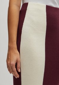 Strickrock mit senkrechten Streifen in Bordeauxrot und Creme, glatte Textur, hoher Bund, figurbetonte Silhouette und ohne sichtbare Beschläge.