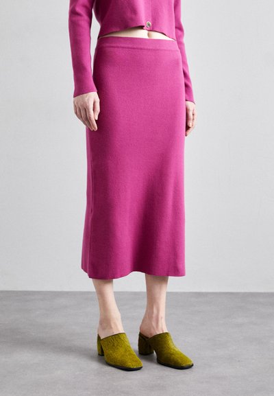 Fustă tricotată fucsia cu o siluetă dreaptă și un elastic la talie, asociată cu pantofi verde texturat tip slip-on cu toc pătrat.
