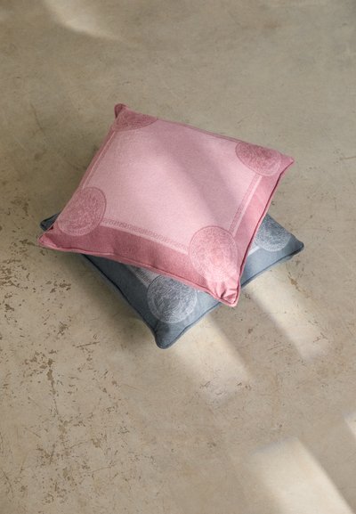 Two square cushions: one pink with circular patterns, the other gray featuring similar design. Soft fabric on a textured surface.