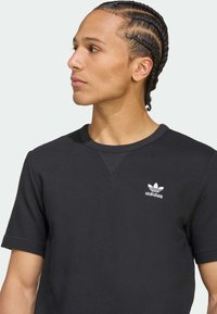 Μαύρο κοντομάνικο υφασμάτινο πουκάμισο με στρογγυλή λαιμόκοψη και λευκό λογότυπο Adidas στο αριστερό στήθος.