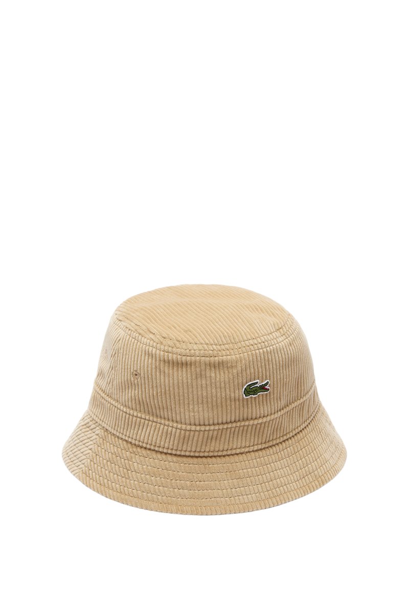 Cappello a secchiello in corduroy beige con una visiera stretta. Presenta un logo di coccodrillo verde ricamato sul lato. Superficie testurizzata ondulata.