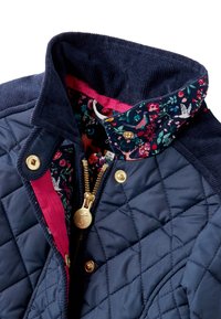 Chaqueta de navy acolchada con cuello de pana, forro con estampado floral, cremallera dorada y botones de presión; presenta acentos en rosa contrastantes.