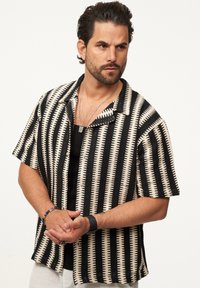 Kurzarmhemd mit einem schwarz-elfenbeinfarbenen gestreiften Muster, das dreieckige Akzente und eine lässige Passform aufweist. Mit Knopfverschluss und Kentkragen.