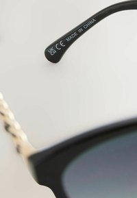 Mustad prillid julge disainiga. Templi osas on kuldne kettjaoline tekstuur ning vasakul käel on märgised 'CE' ja 'MADE IN CHINA'.