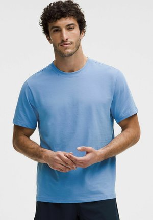 T-shirt azzurro chiaro a manica corta realizzato in morbido cotone, con collo rotondo classico e dettagli di cucitura minimi, indossato da un modello in piedi.