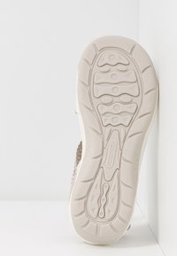 Helle beigefarbene Sneaker-Sohle mit einer strukturierten, geformten Gummibeschichtung. Verfügt über ein wellenförmiges Profilmuster und ein eingeprägtes Logo. Flache und leicht erhöhte Kanten.