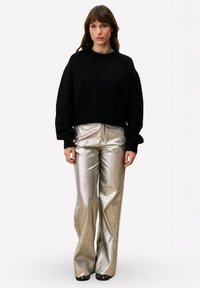 Zwarte, pluizige cropped trui gecombineerd met glanzende zilveren flare broek. De trui heeft lange mouwen; de broek heeft een glad, metallic uiterlijk.