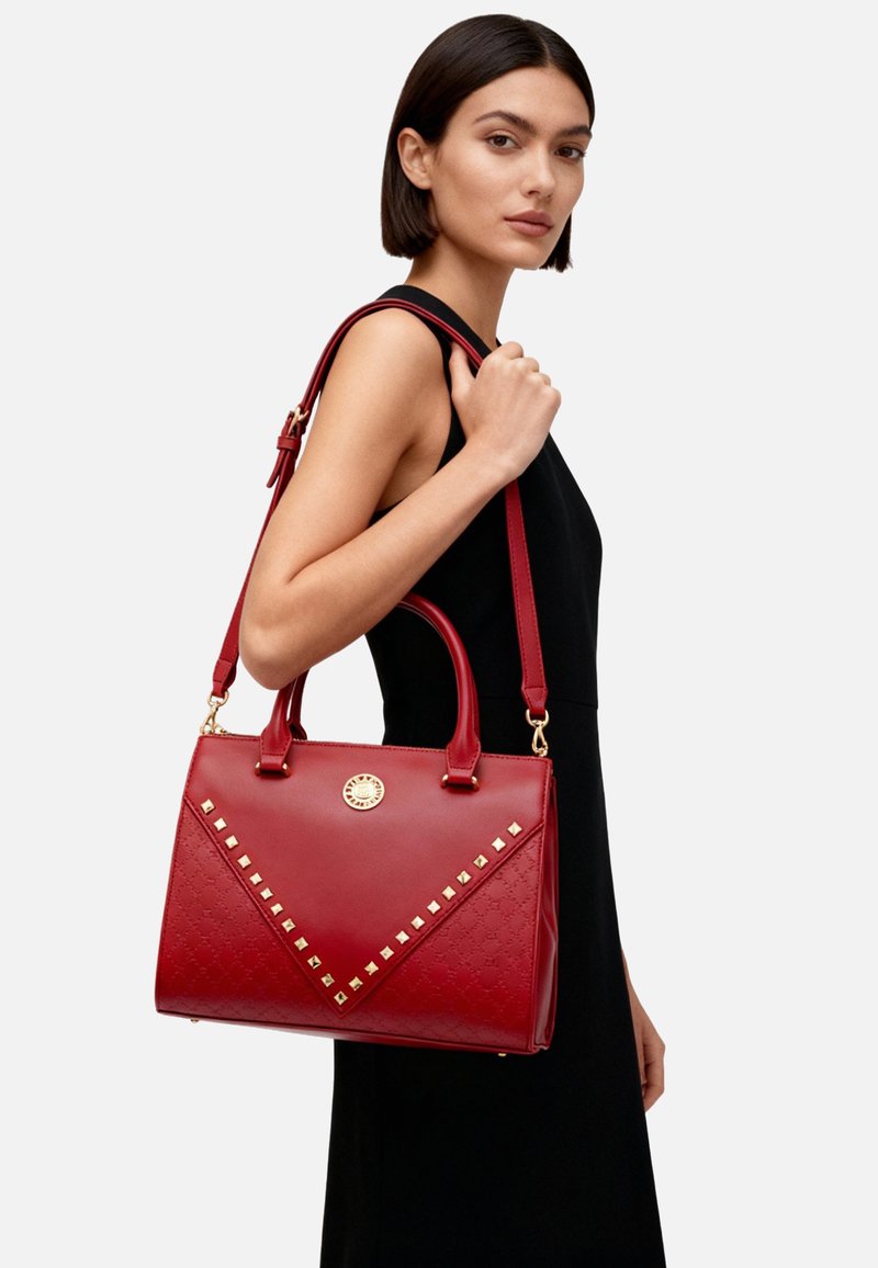 Borsa a mano in pelle rossa con forma strutturata, ferrature dorate e borchie a piramide. Dotata di doppi manici e tracolla rimovibile.