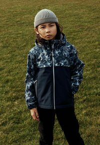 Veste à capuche avec un haut en camouflage bleu et une partie inférieure en navy uni. Fermeture à glissière, poignets élastiques et deux poches latérales.