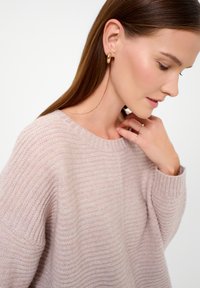 Light pink ribbed knit sweater with a round neckline. Model wears gold hoop earrings. Soft texture, relaxed fit, long sleeves.