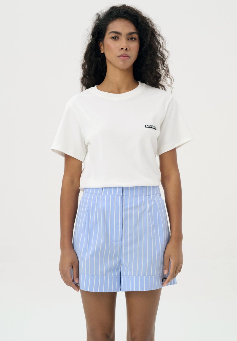 Biała bawełniana koszulka z czarnym logo, w połączeniu z jasnoniebieskimi szortami w paski z plisowanym wzorem i podwiniętym dołem.