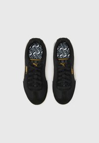 Zapatillas deportivas negras con materiales de malla y ante, que presentan detalles en dorado y cordones negros, diseñadas con una plantilla estampada.