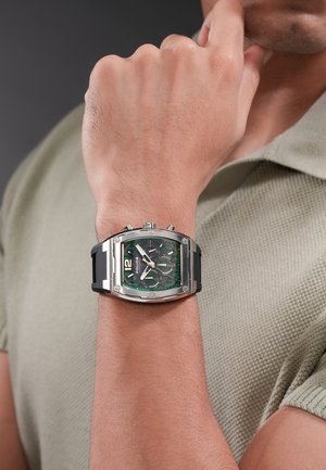 Primer plano de una muñeca que lleva un reloj cronógrafo de la marca Police en verde y plata con correa y pulsadores negros.