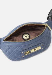 Blå quiltad läder Love Moschino bältesväska med guldfärgad dragkedja och logoplatta, delvis öppen för att visa det mönstrade bruna innerfodret.
