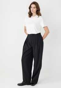 Biała koszulka z okrągłym dekoltem zestawiona z czarnymi spodniami w prążki o wysokim stanie, z paskiem i plisowanym przodem. Czarne loafersy dopełniają stylizację.