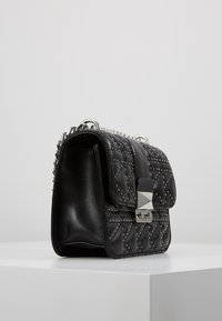 Borsa a tracolla in pelle nera trapuntata con borchie in argento, forma rettangolare, tracolla a catena e chiusura in metallo. La superficie testurizzata crea un contrasto con gli accenti lisci.